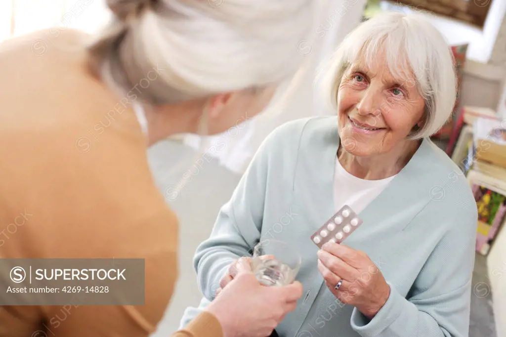 Woman helping elderly woman taking medicine.