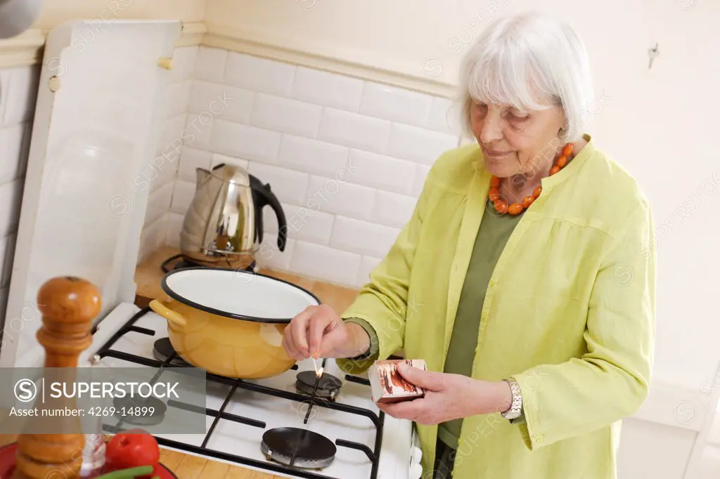 Elderly woman lighting gas burner.