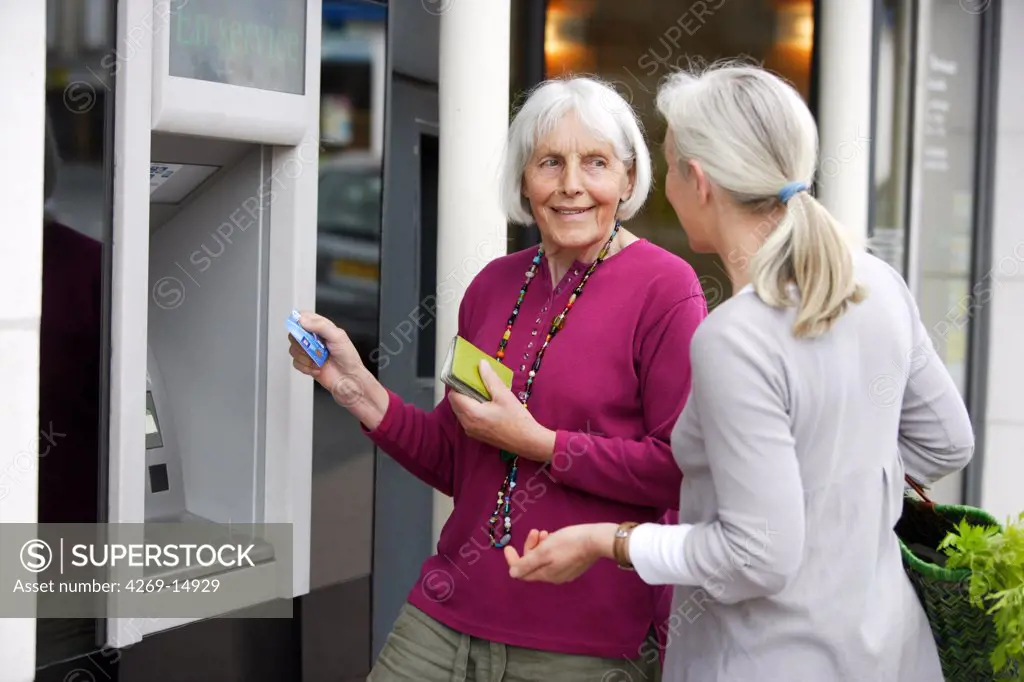 Person helping elderly woman withdrawing money from cash machine.