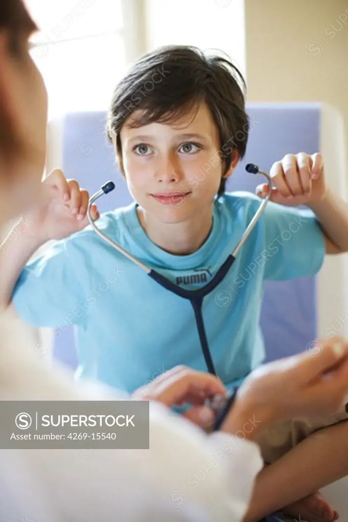 9 years old boy playing with a stethoscope during medical consultation.