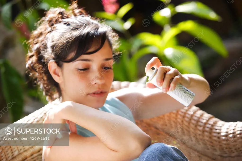 Young woman applying spray against insect bites and itching on her arm.