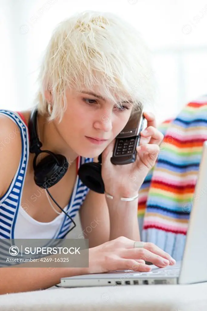Teenage girl using laptop computer and cell phone.