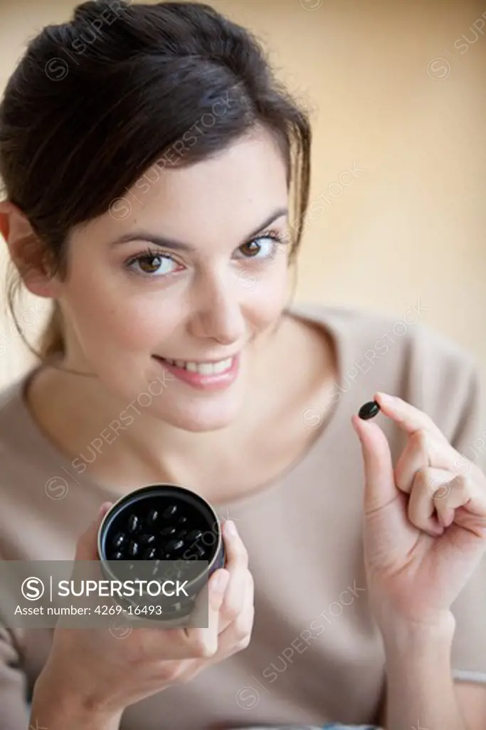 Woman taking capsules of officinal charcoal treated to increase its absorption capacity, used to releive heavy digestion or as treament for aerophagia.