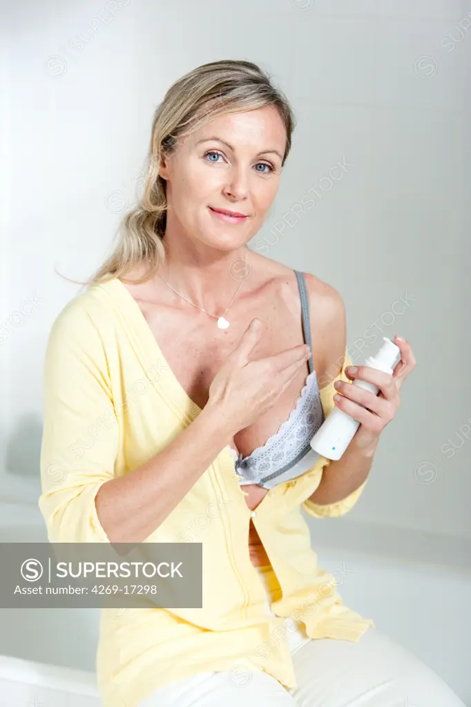 40 years old woman applying antiwrinkle or moisturizing cream on her low neckline.