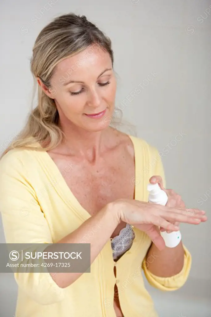 Woman applying an estrogen gel on her hands for a Hormone Replacement Therapy, in order to releive the undesirable effects of menopause.