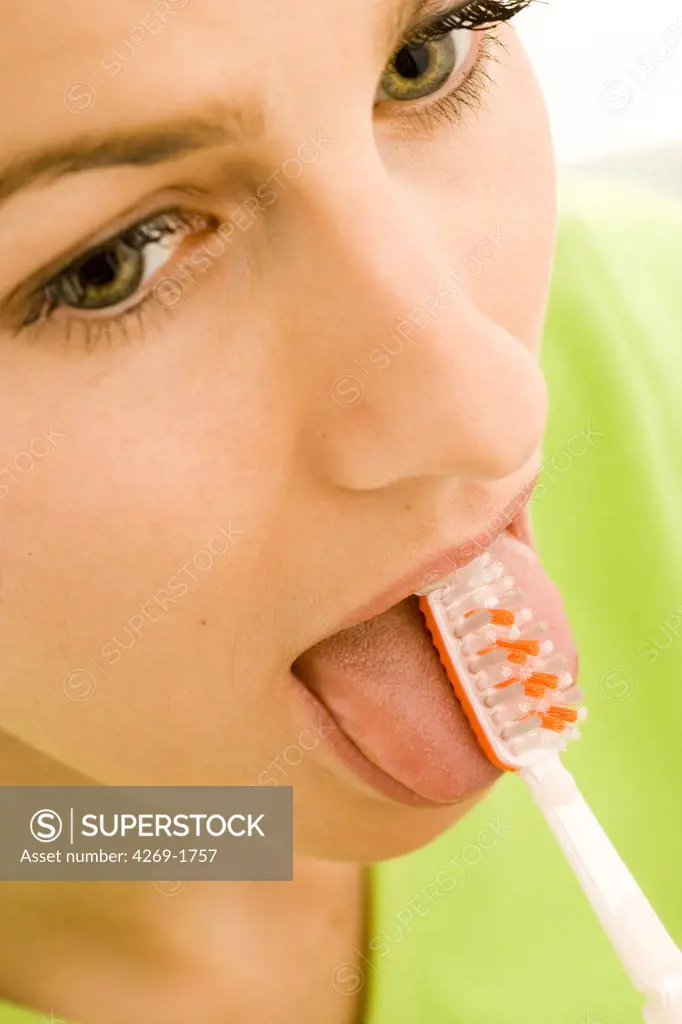 Woman brushing her tong with a double side toothbrush to eliminate the bacteria of the tongue responsible for bad breath.