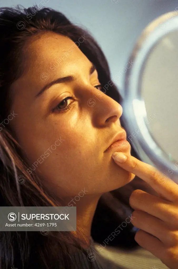 Woman checking her face in the mirror, for acnea pimples or other skin problems.