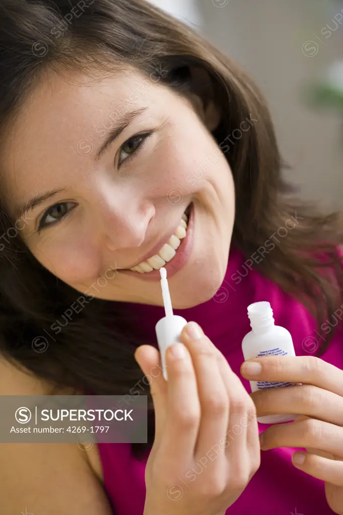 Woman applying a bleaching gel on her teeth.