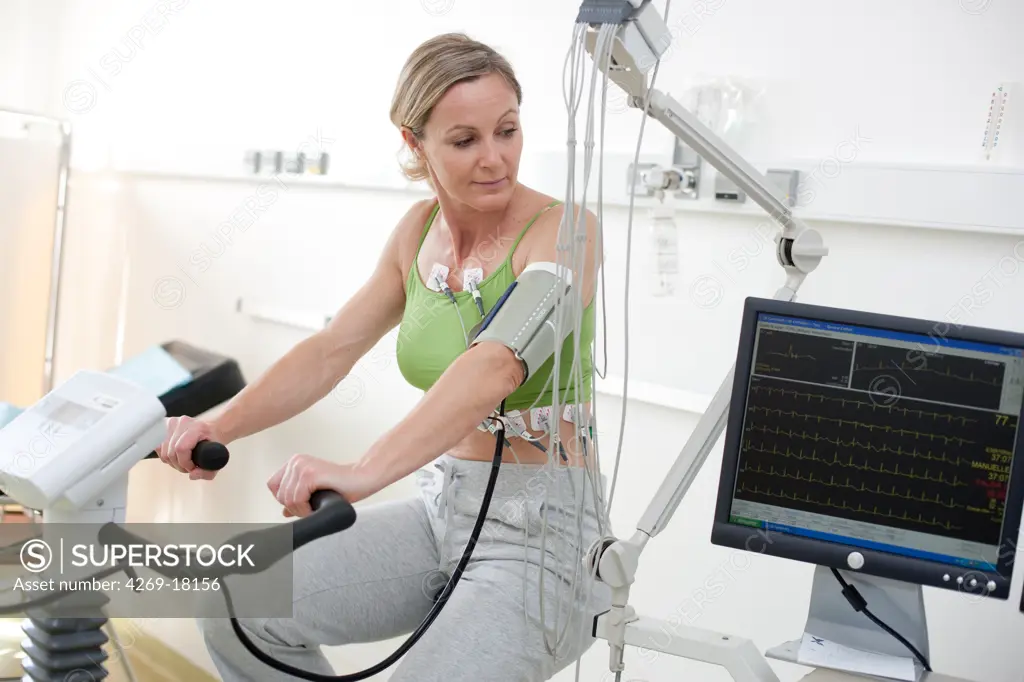Patient doing monitored heart rehabilitation training exercises on ergometric bicycle. Limoges hospital, France.
