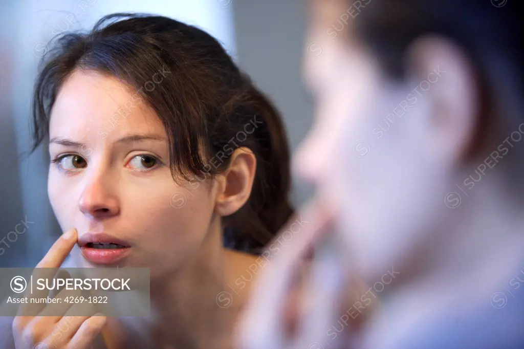 Woman checking her face in the mirror, for acnea pimples or other skin problems.