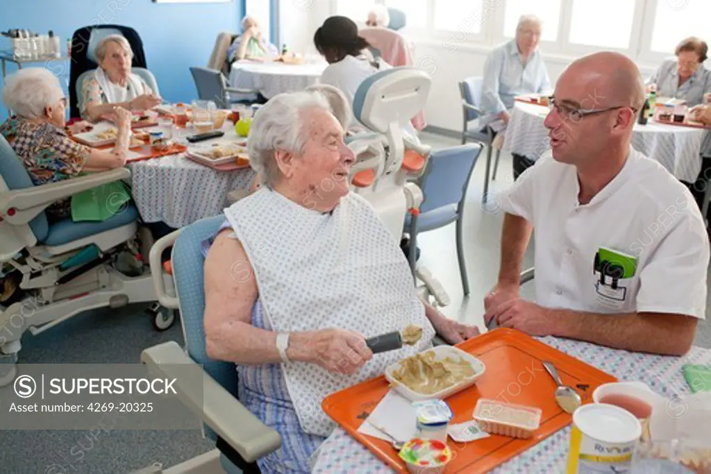 Medico-psychological assistant helping an alzheimer's disease person to learn again gestures to eat independently with an adapted spoon. Residential home for dependent elderly person, Limoges, France.
