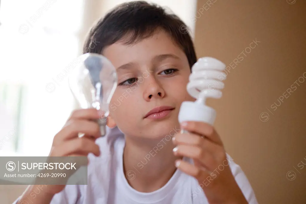 Boy holding energy saving lightbulb (right) and incandescent lightbulb (left).