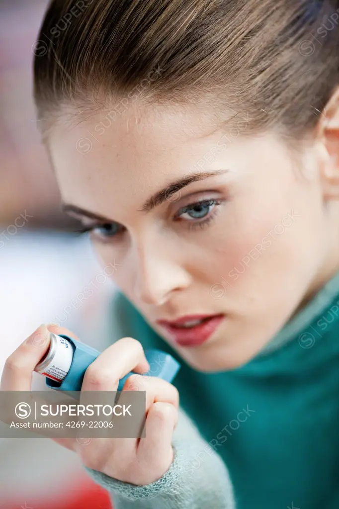 Woman using an aerosol inhaler that contains bronchodilator for the treatment of asthma. The inhaler dilates lungs airways to improve breathing.