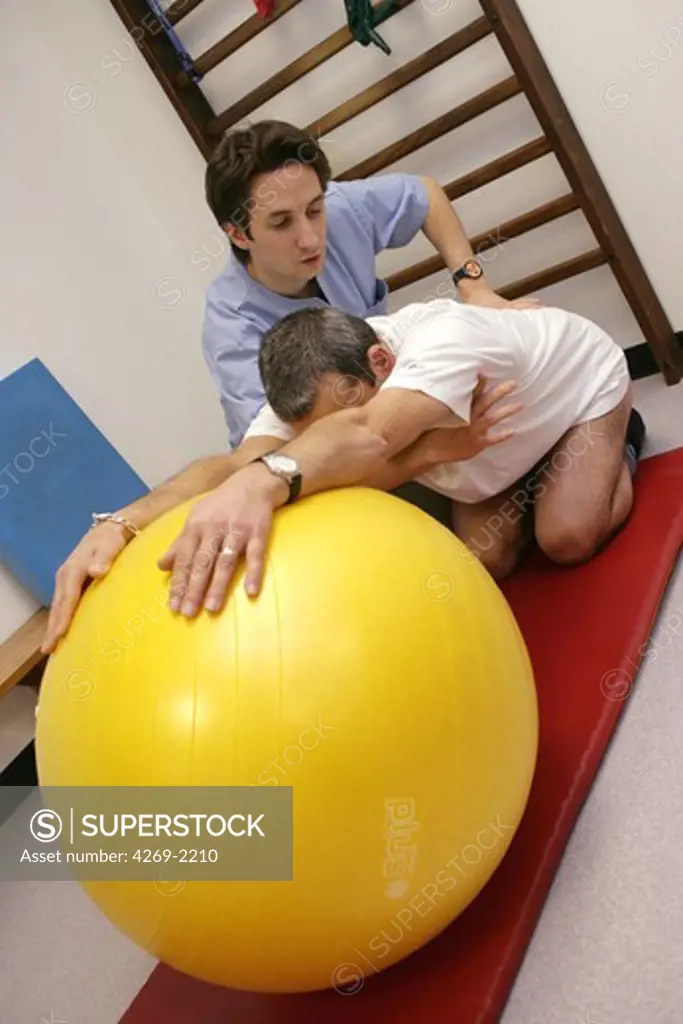 Patient suffering from lower back pain (lumbar pain) practising back-stretching rehabilitation excercises with a physiotherapist.