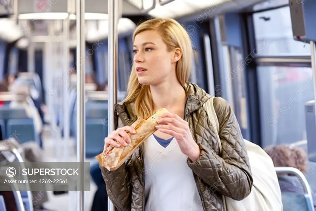 Woman eating a sandwich in the subway.