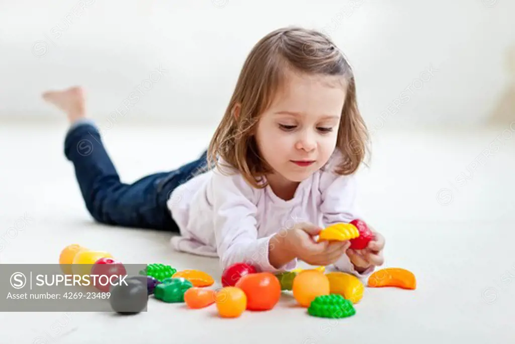 4 years old girl playing with plastic fruits and vegetables.