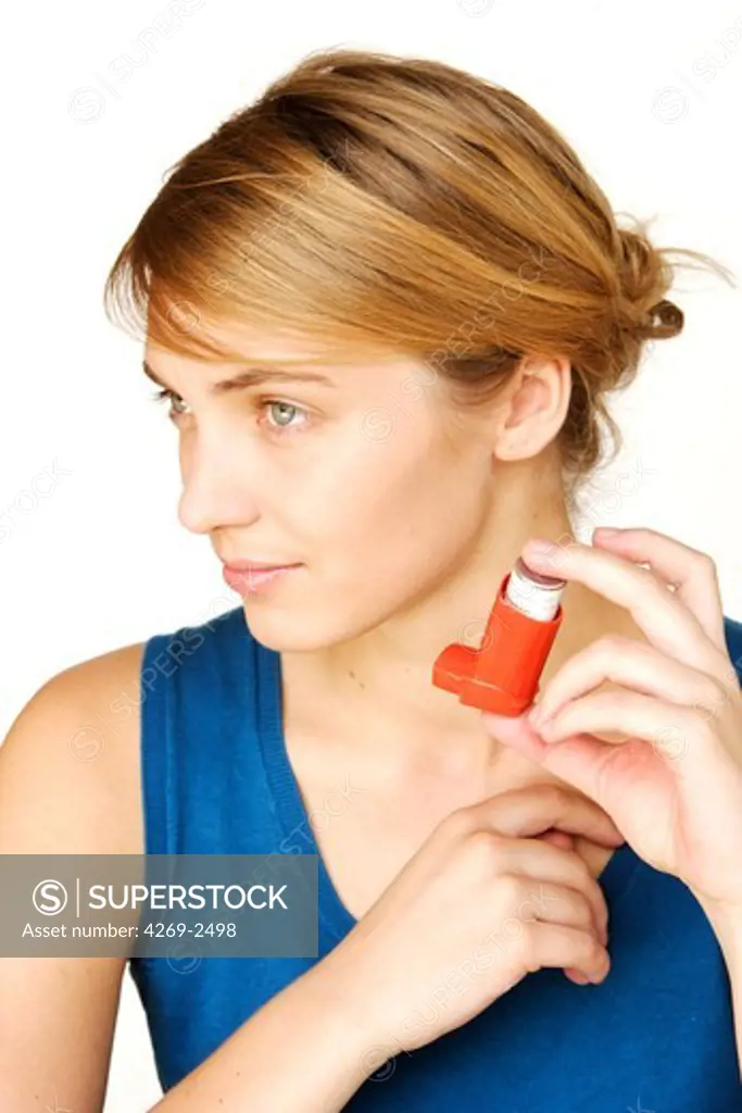 Woman using an aerosol inhaler that contains bronchodilator for the treatment of asthma. The inhaler dilates lungs airways to improve breathing.