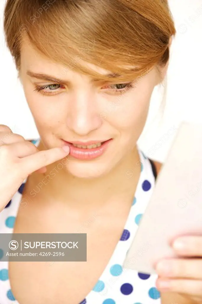 Woman checking her lips for a cold sore in the mirror.