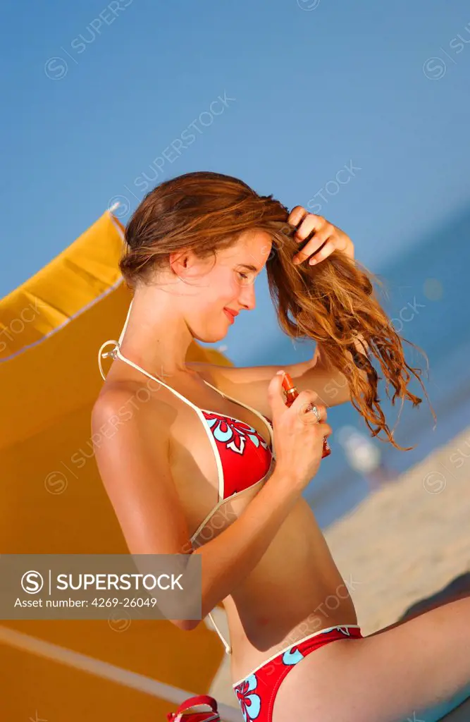 Sun. Woman applying protective oil in spray on her hair at the beach.
