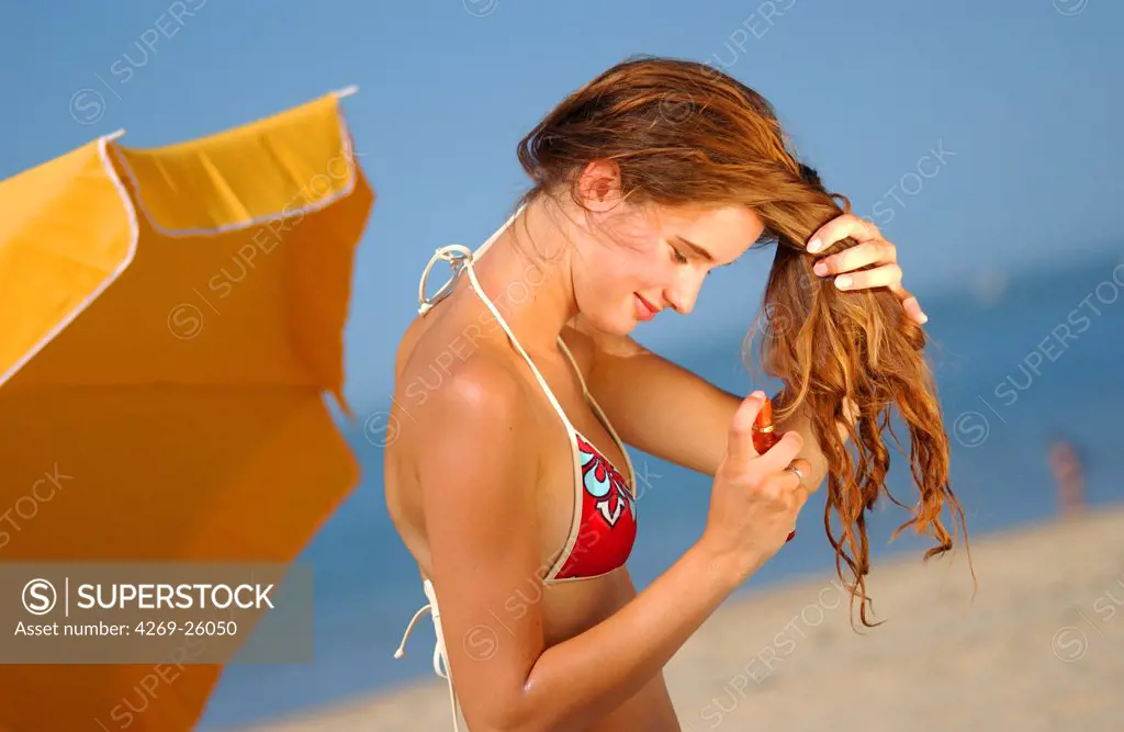 Sun. Woman applying protective oil in spray on her hair at the beach.