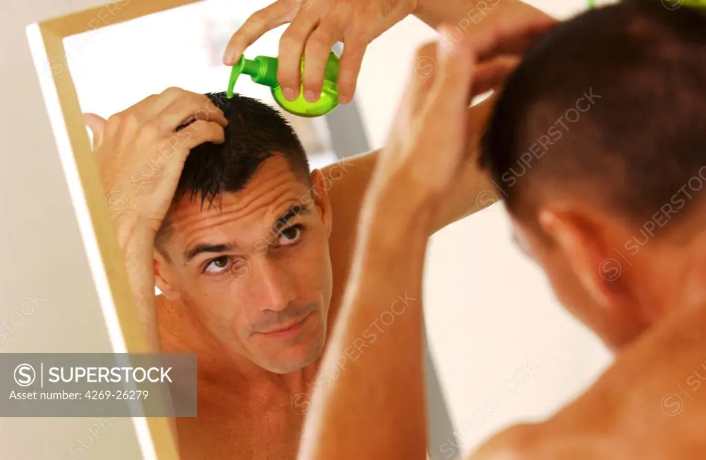 Loss of hair. A man uses hair lotion to prevent loss of hair.