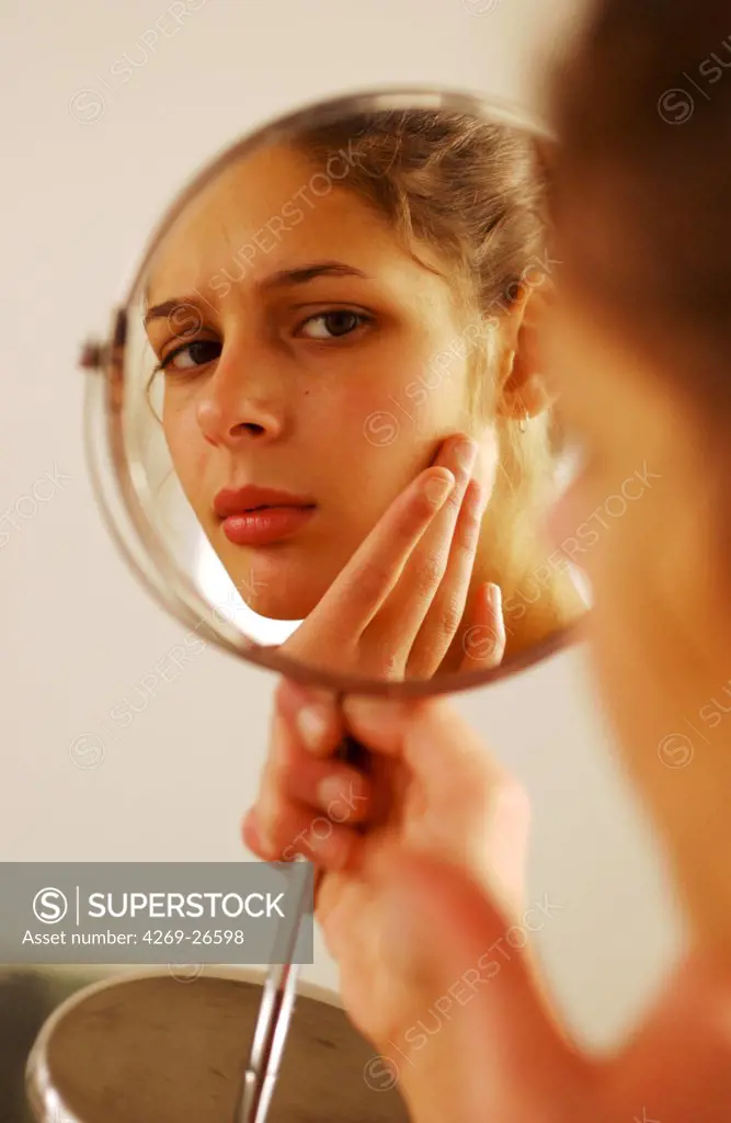 Teenager. Female teenager checking her face in the mirror, for acnea pimples or other skin problems.