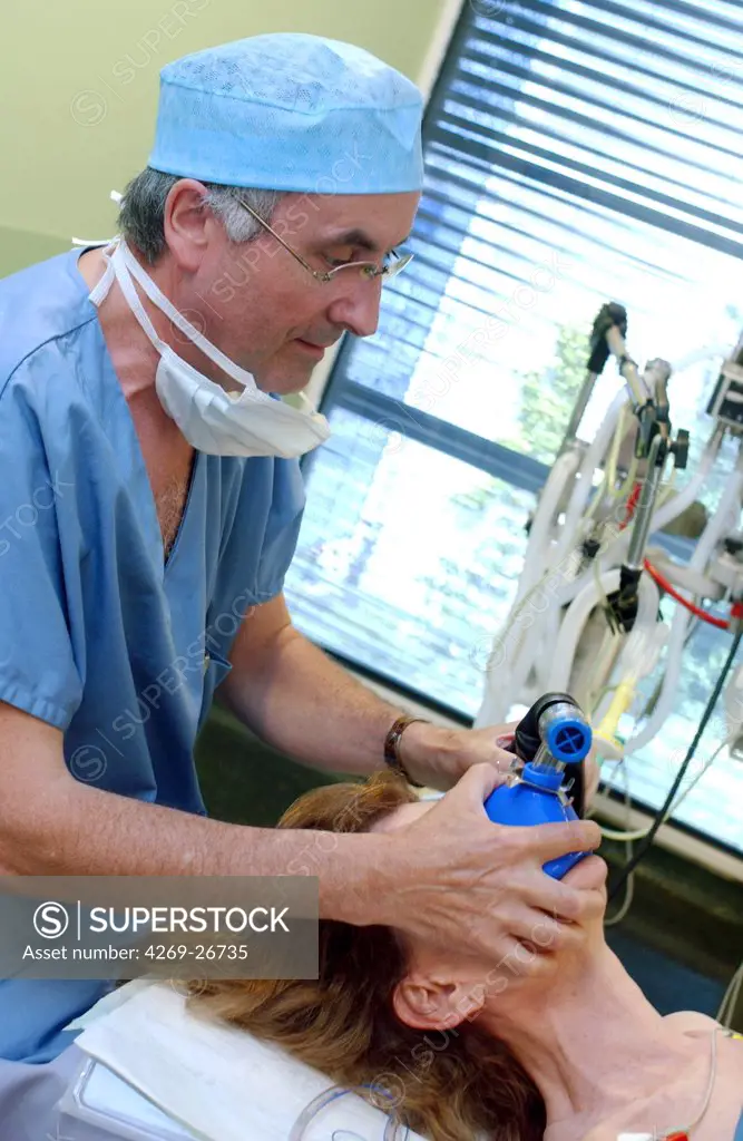 General anesthesia. An anaesthetist have a patient inhaling anesthetic gas from a transparent gas-mask prior to plastic surgery.