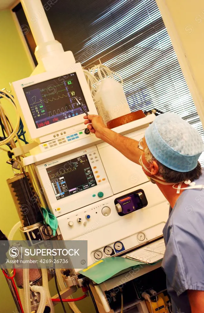 General anesthesia. Anaesthetist in surgical dress beside anaesthetic monitoring equipment during surgery.. The equipment supplies anaesthetic products that maintain the unconsciousness of the patient. The vital signs (heartbeat and breathing) are displayed on a monitor.