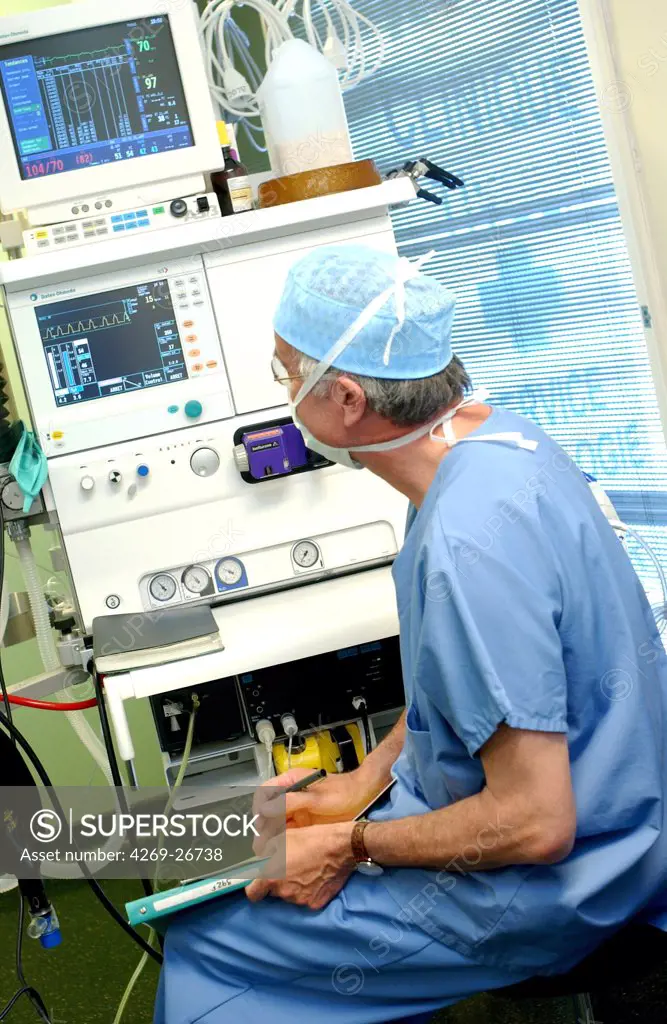 General anesthesia. Anaesthetist in surgical dress beside anaesthetic monitoring equipment during surgery. The equipment supplies anaesthetic products that maintain the unconsciousness of the patient. The vital signs (heartbeat and breathing) are displayed on a monitor.