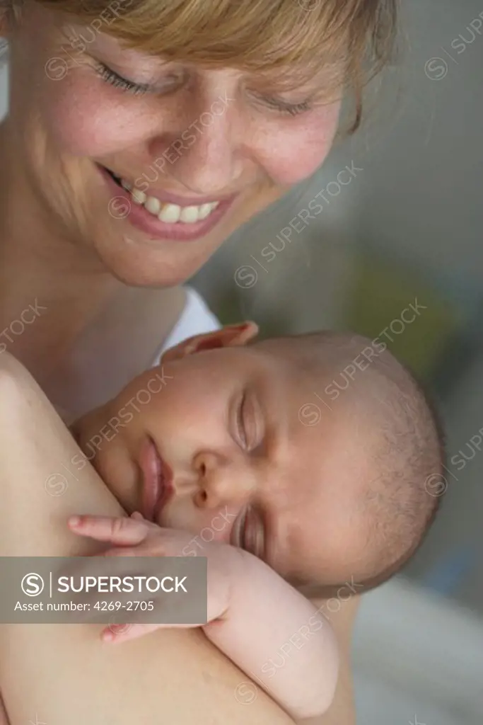 2 months old baby sleeping in the arms of her mother.