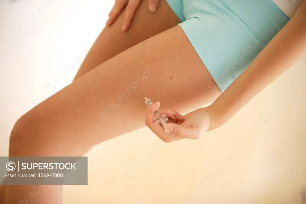 Woman giving herself injection of epinephrine (adrenaline) in her thigh, an emergency treatment in case of anaphylactic or anaphylactoid shock (allergies to drugs, food or insects bites).