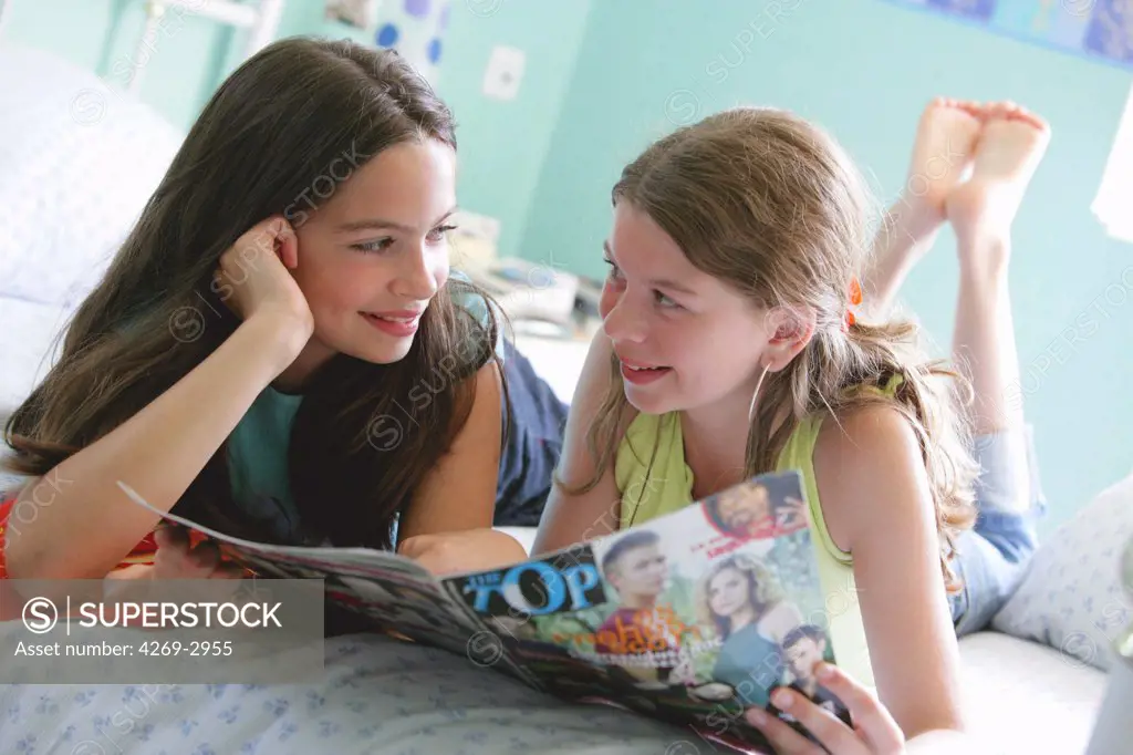 Two 11 and 12 years old sisters reading a magazine.