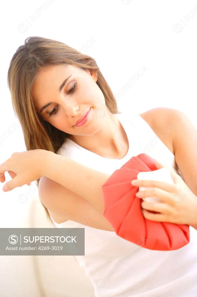 Woman treating pain in the elbow with a hot-water bag (thermotherapy) or with ice bag (cryotherapy).