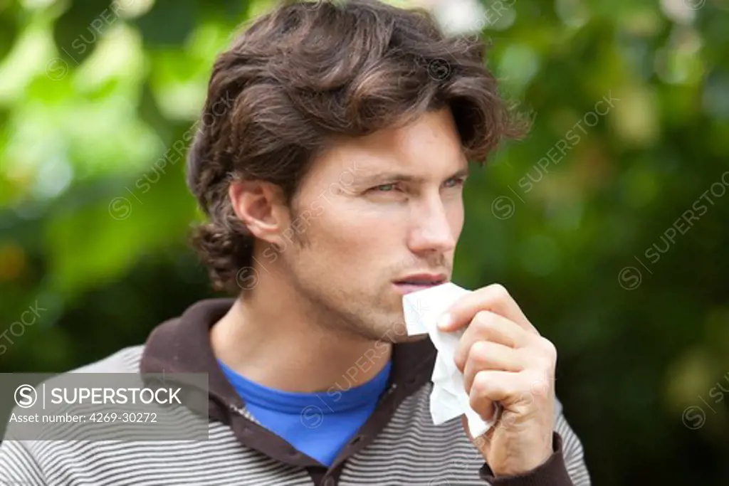 Man with a common cold blowing his nose with a tissue
