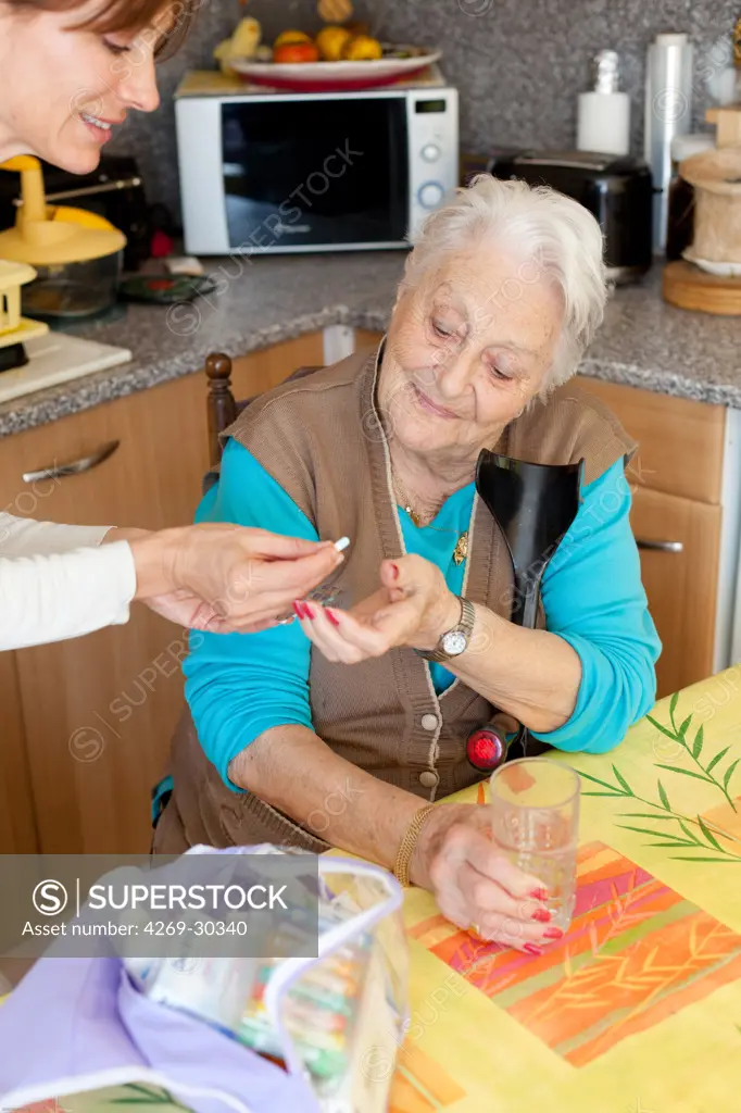 Woman assisting 94 years old woman taking medication.
