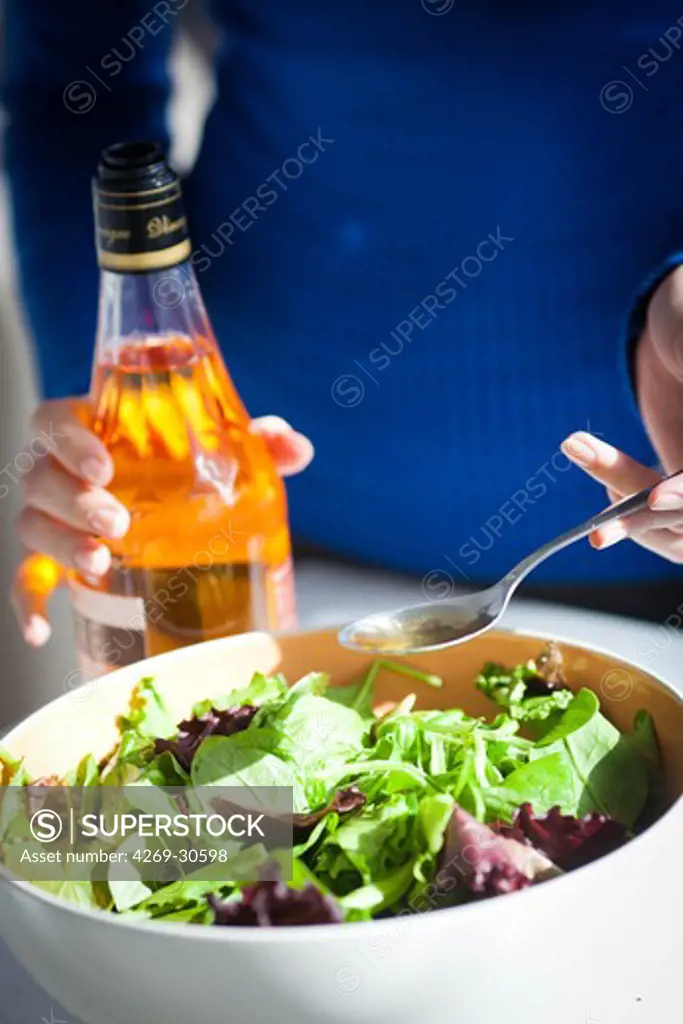 Food. Woman adding cider vinegar on a salad.