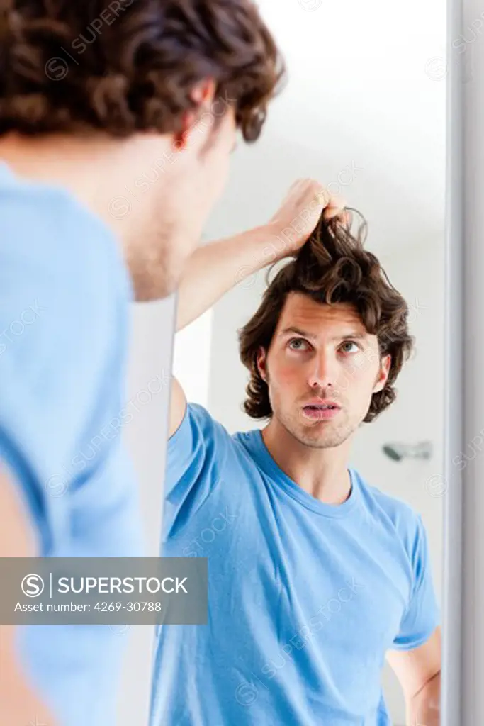 Loss of hair. Man inspecting his hair in a mirror.