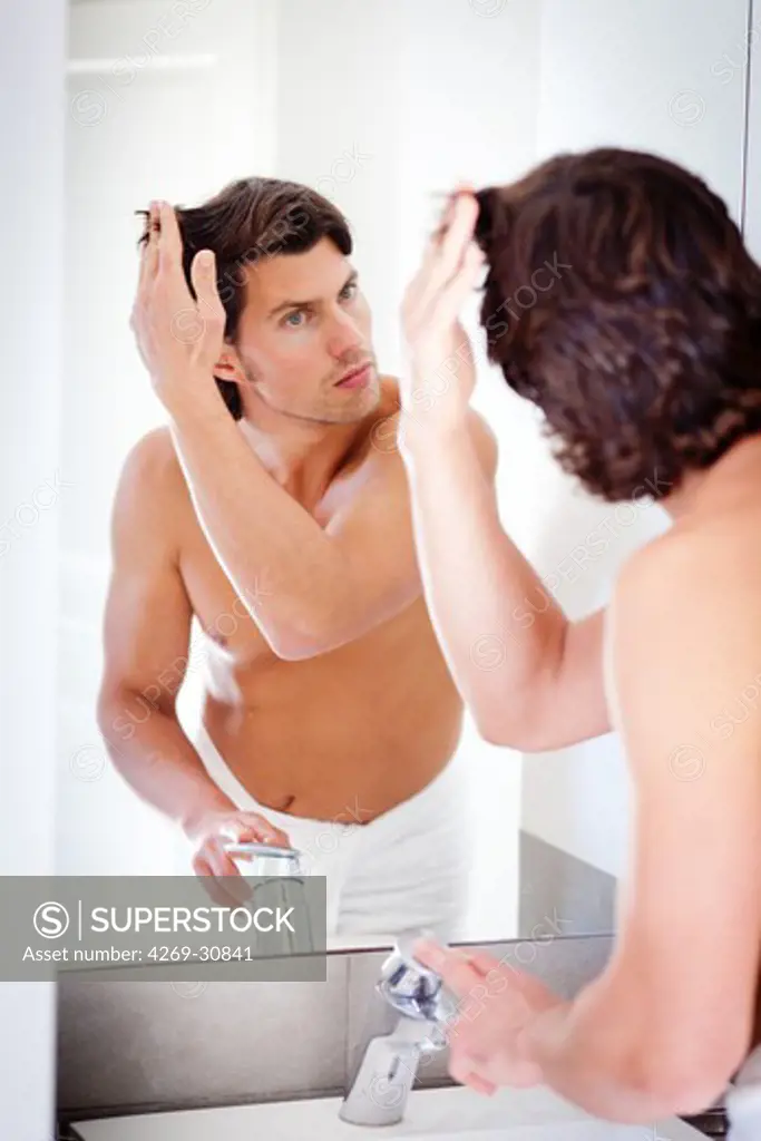 Loss of hair. Man inspecting his hair in a mirror.
