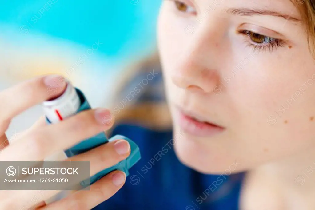 Asthma. Woman using an aerosol inhaler that contains bronchodilator for the treatment of asthma. The inhaler dilates lungs airways to improve breathing.