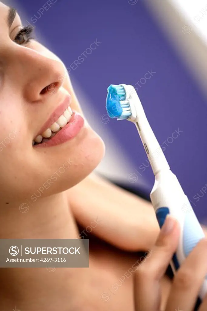 Woman brushing her teeth with electric toothbrush.