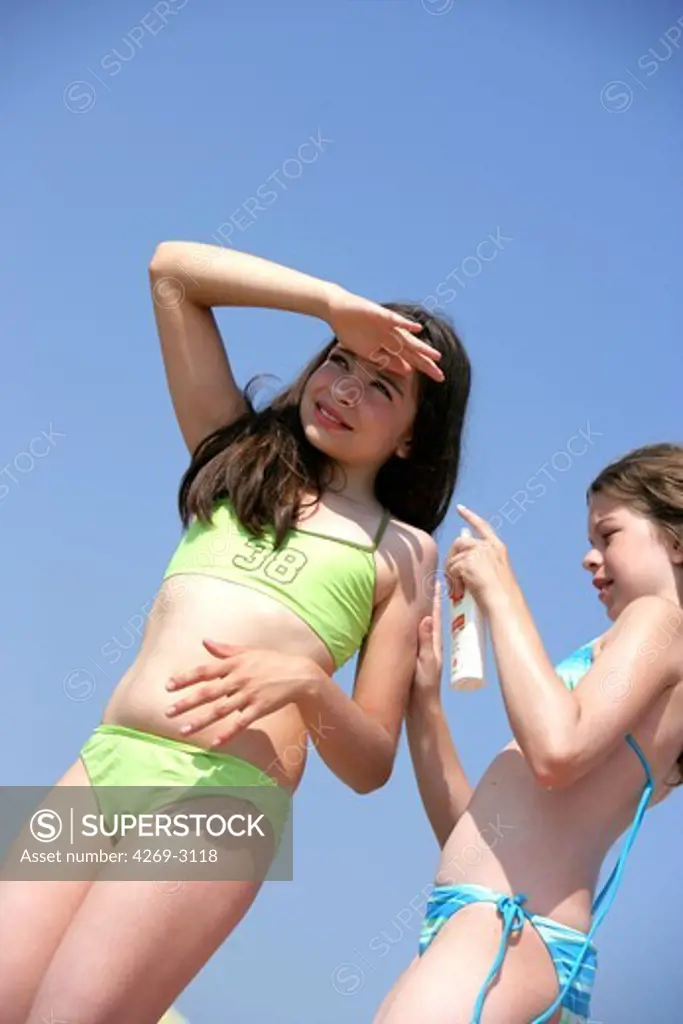 Teenage girl applying sunblock on her friend's back at the beach.
