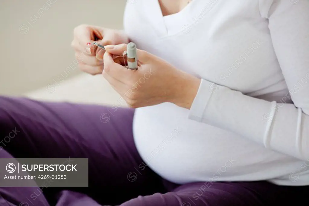 A diabetic pregnant woman is checking her blood sugar level (self glycemia). A drop of blood obtained with a pen-like lancing device is placed on a test stick and analysed with blood glucose tester (glucometer).