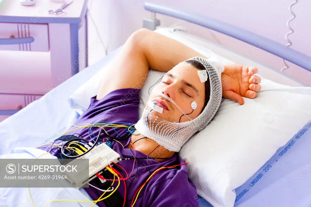 Man undergoing a polysomnographic examination. The polysomnography is the study of the physiological activity of the body during sleep, and includes the measurement of the lungs, heart and brain activity. The interpretation of these recordings can reveal disfunctions like sleep apnea, snoring, hypersomnia, insomnia... Limoges hospital, France.