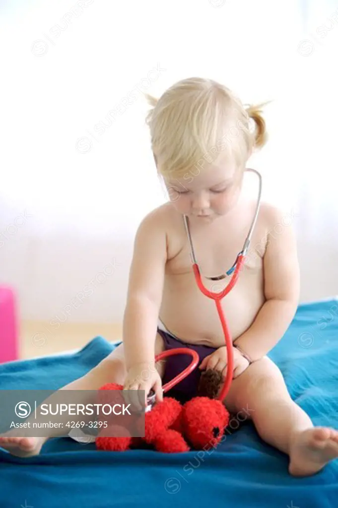 18 months old baby girl examining her teddy bear with a stethoscope.