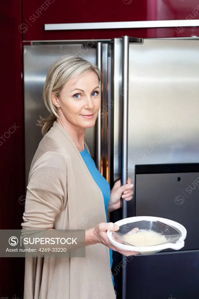 woman putting a plate of food inside a refrigerator.
