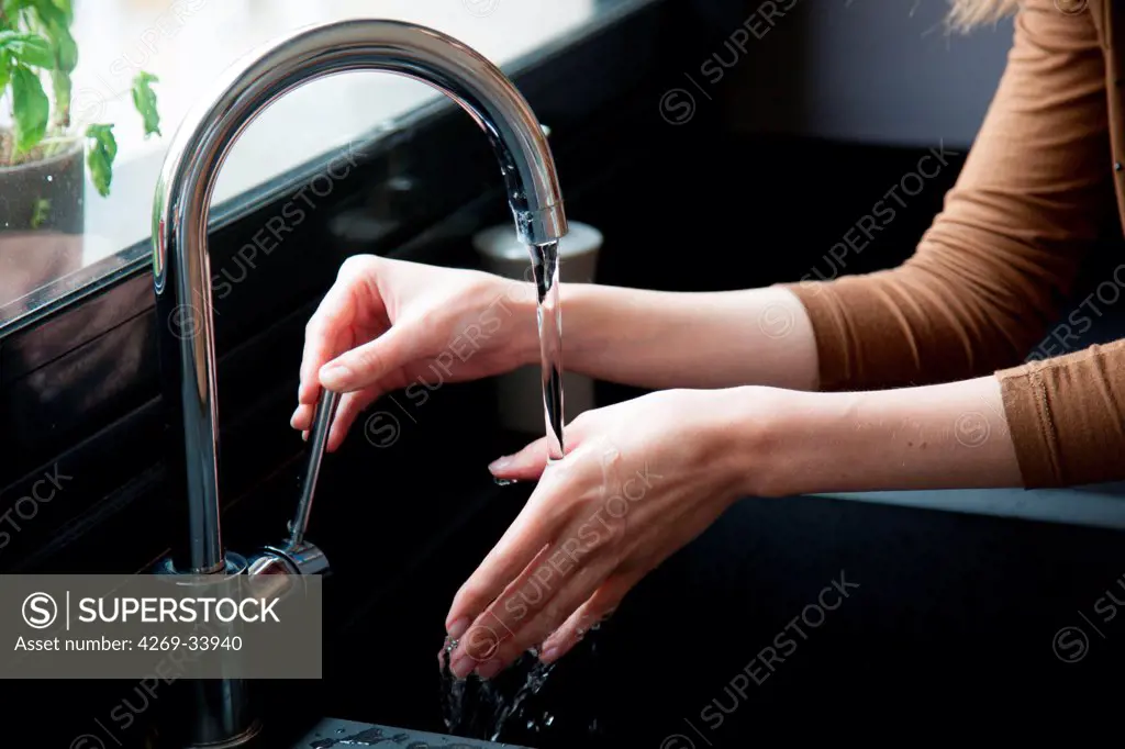 Woman treating superficial hand burn with cold water.