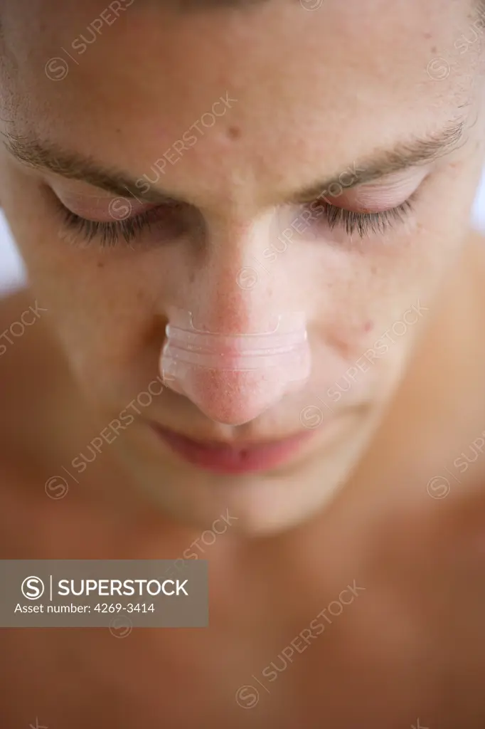 Man wearing a nasal strip, intended to provide relief from rhinitis, hay fever and common colds by allowing a clear passage of the air through the nostrils.