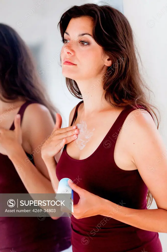 Woman applying antiwrinkle or moisturizing cream on her low neckline.