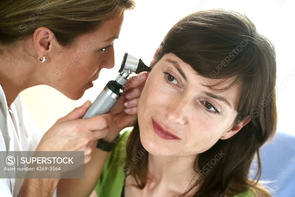 Female doctor examining the ears of a female patient with an otoscope.