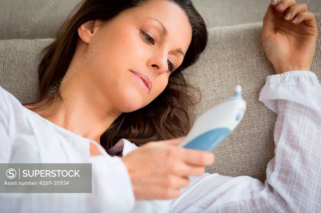 Woman taking her temperature with a digital tympanic thermometer